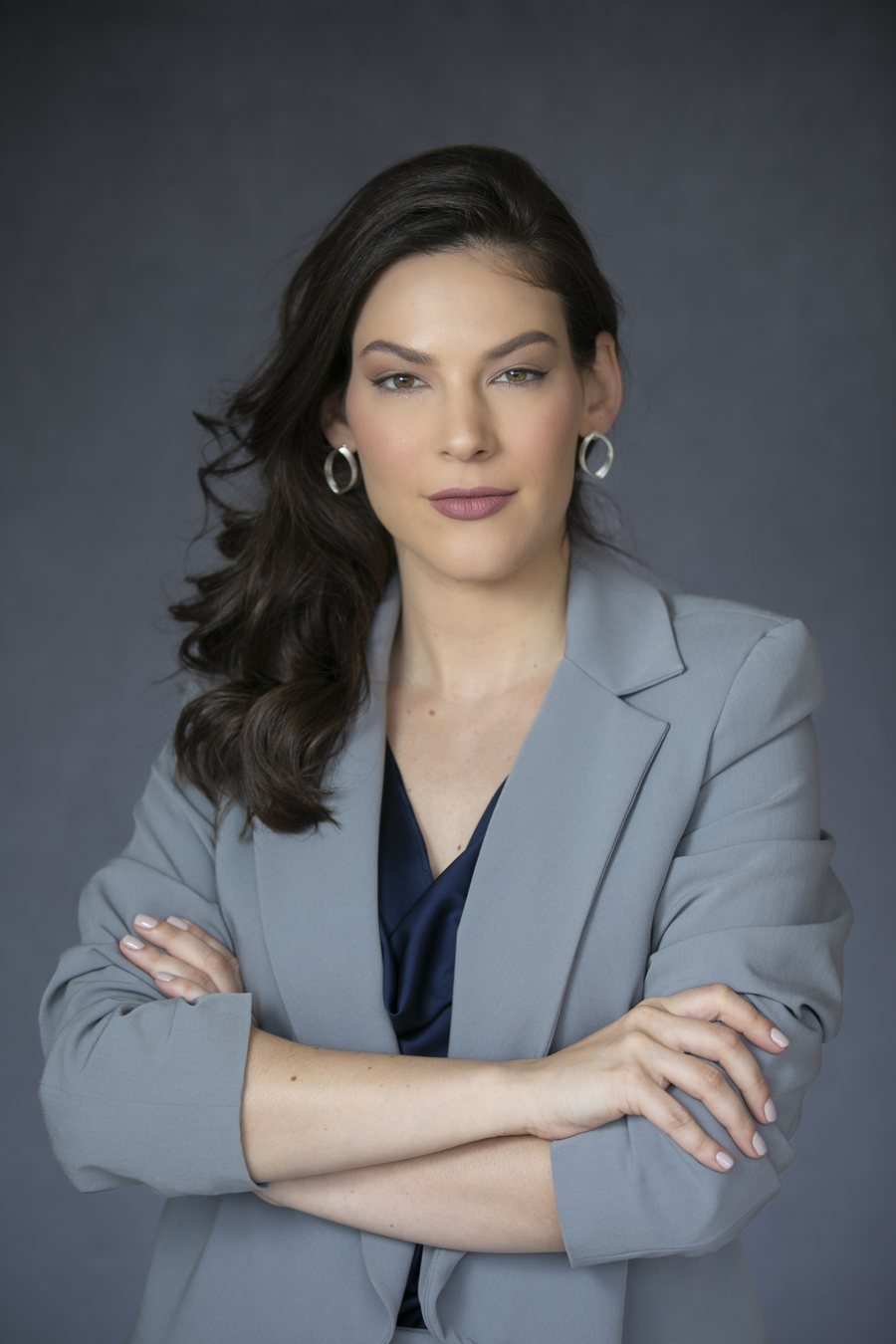 Dra. Lisandra Lisboa, de blazer cinza e braços cruzados